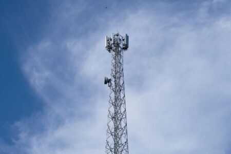 Une haute tour de télécommunications métallique se dresse sur fond de ciel bleu clair parsemé de nuages ​​épars.
