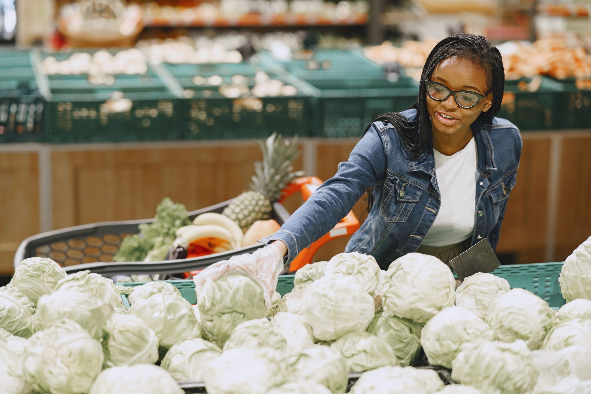 Une femme souriante choisissant des choux dans le rayon primeur d’un supermarché.